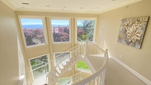 Un intérieur spacieux avec un escalier en colimaçon blanc, de grandes fenêtres donnant sur la verdure et un tableau accroché au mur.
