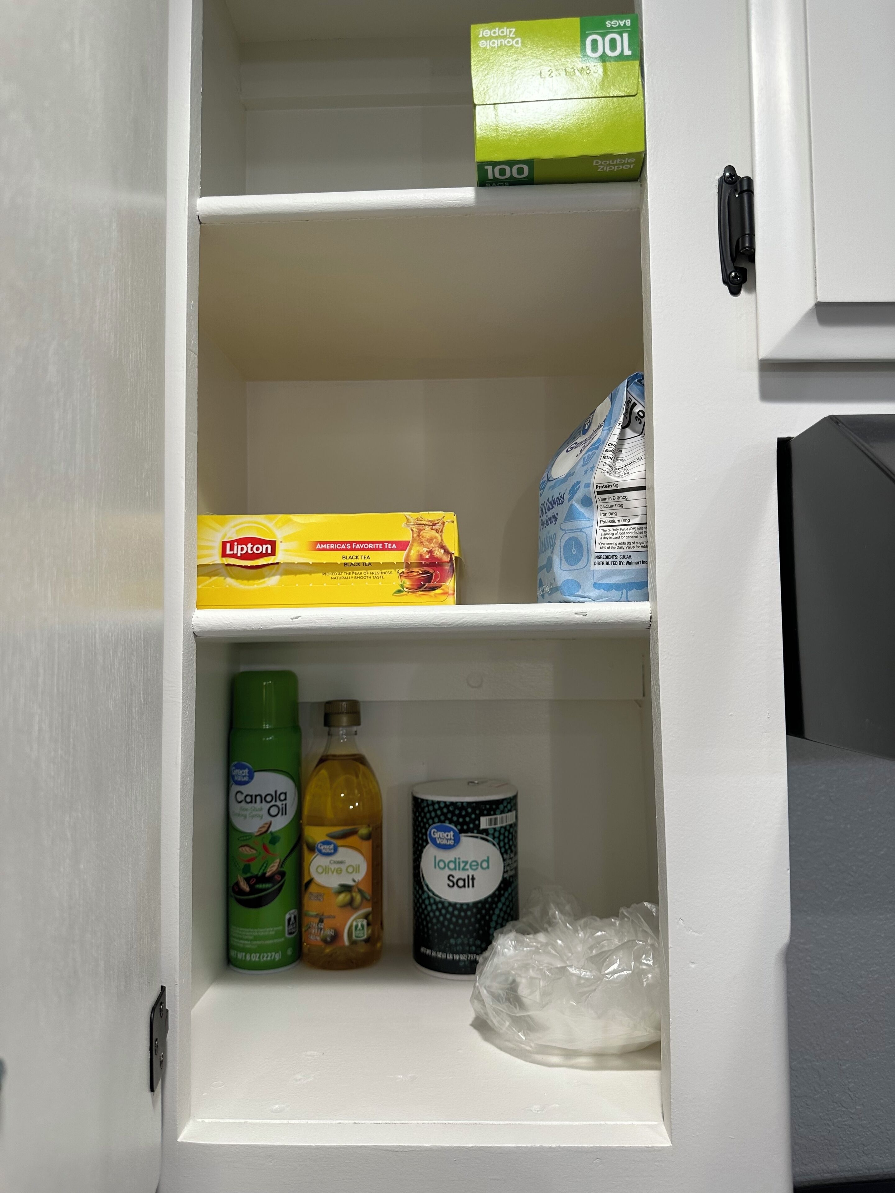 A pantry with a box of Lipton black tea, a bag of Arm & Hammer baking soda, a bottle of Canola Oil, a bottle of Olive Oil, a container of iodized salt, and a plastic bag.