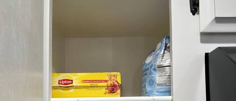 A pantry with a box of Lipton black tea, a bag of Arm & Hammer baking soda, a bottle of Canola Oil, a bottle of Olive Oil, a container of iodized salt, and a plastic bag.