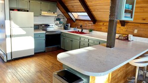 Una cocina con refrigerador, estufa, pileta y techo de madera.