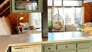 Una cocina con lavavajillas incorporado, una silla colgante y ventana con vistas a un jardín.