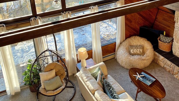 Un acogedor loft con techos altos, ventanas amplias, una silla colgante, un sofá y una mesita.
