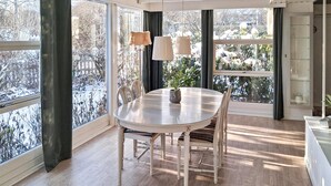 Un comedor con una mesa redonda, sillas e iluminación colgante. Amplias ventanas ofrecen vistas a un paisaje nevado.