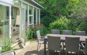 A patio with wicker furniture, a glass door leading to a room, and lush greenery.