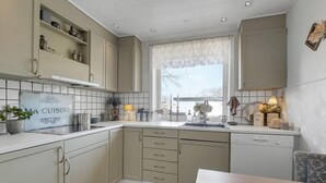 Una cocina moderna con armarios color crema, una ventana con cortinas de encaje y un lavavajillas Bosch.