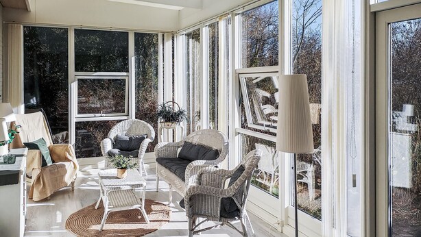 Un solarium con muebles de mimbre, ventanas amplias y una lámpara de pie.