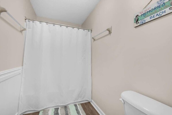 Un baño con cortina de ducha blanca, alfombra a rayas y un inodoro.