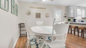 A dining area with a white table and chairs, a ceiling fan, and a kitchen in the background.