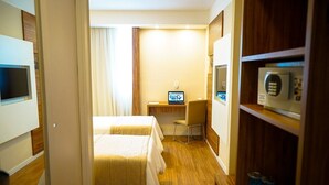 Ein Hotelzimmer mit zwei Betten, einem Schreibtisch mit Computer, einem Sessel und einer Mikrowelle auf einem Regal.