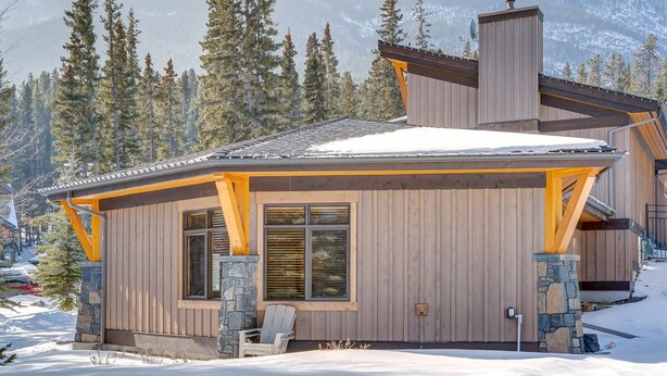A wooden cabin with a stone foundation, large windows, and a chimney. - A Peaceful Mountain Retreat in one of Banff's Most Elegant Homes (Banff)