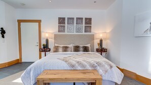 A bedroom with a large bed, two bedside tables, a bench, a door, and a wall with four decorative panels. - A Peaceful Mountain Retreat in one of Banff's Most Elegant Homes (Banff)