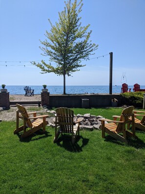 A grassy outdoor area with wooden Adirondack chairs, a small fire pit, and a view of the ocean. - CJs Lakehouse is 1km to Point Pelee. Huge yard, firepit, pets welcome! (Leamington)