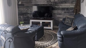 Un salon moderne avec un téléviseur, des canapés en cuir, un tapis à motifs et un mur en bois.
