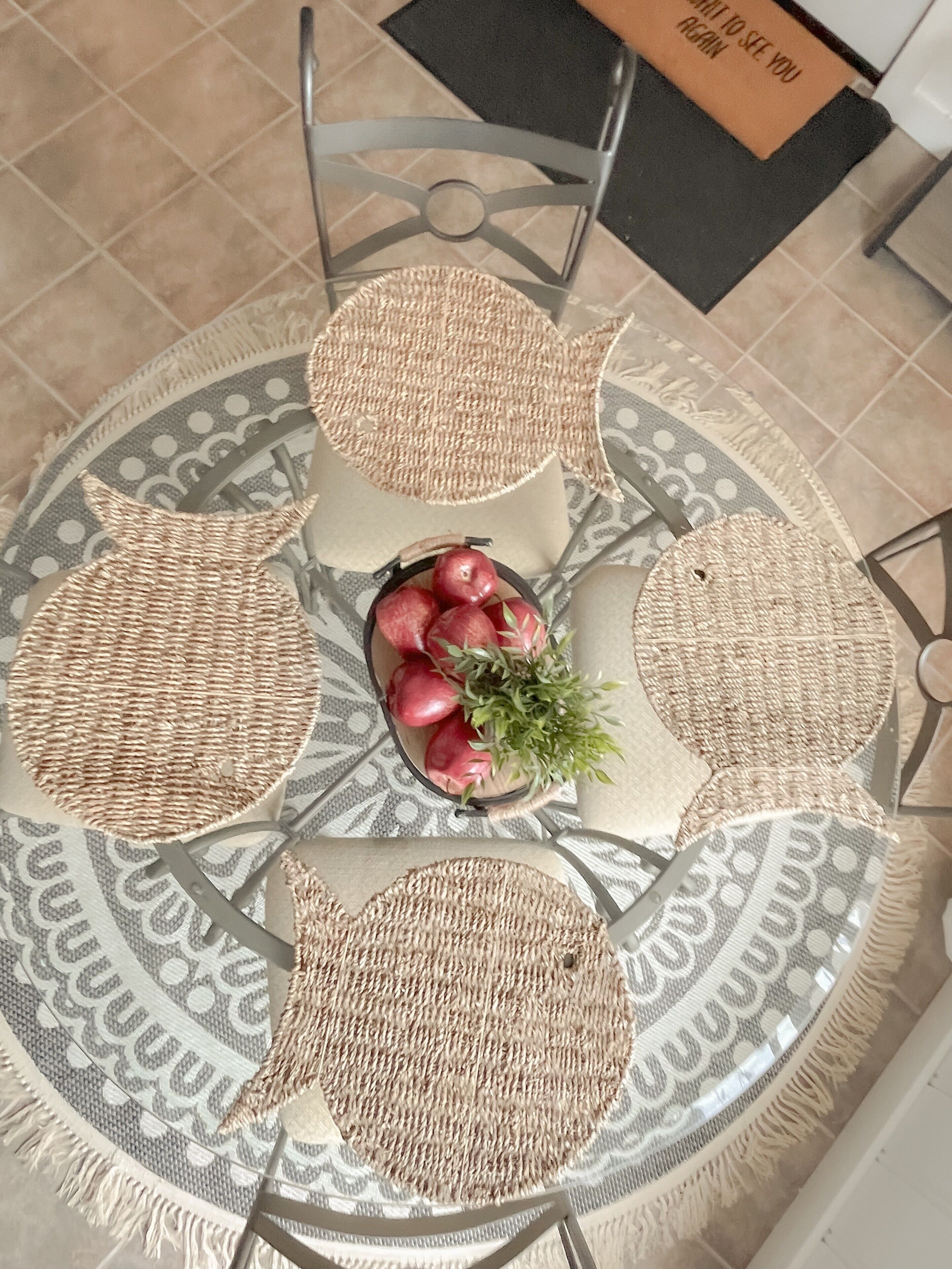 A round table with woven placemats and a central decorative bowl with apples and greenery.
