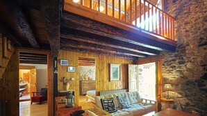 Interior acogedor de una cabaña con piso de madera, un sofá con cojines estampados, una mesa de comedor y una pared de piedra.