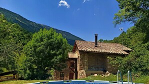 Un edificio de piedra con techo de tejas y una piscina delantera.