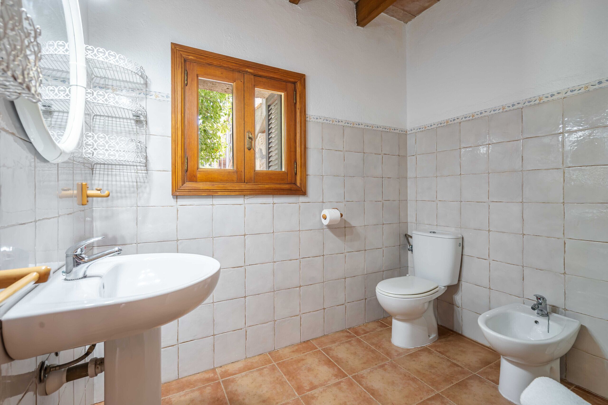 Une salle de bain équipée d’un lavabo, de toilettes, d’un bidet et d’une fenêtre avec un cadre en bois.