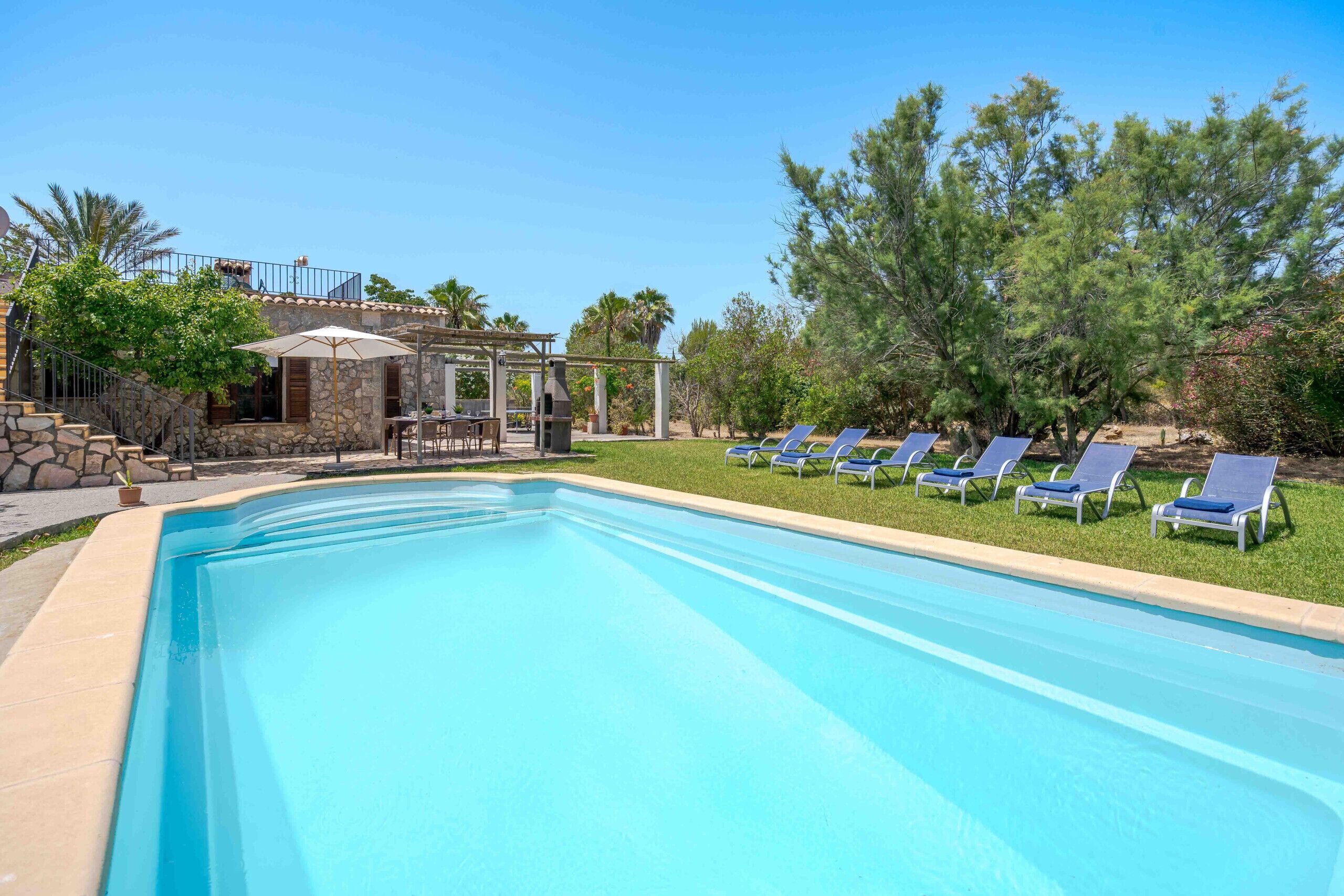 Une piscine avec des chaises longues, un espace barbecue et un bâtiment en pierre agrémenté d’une pergola.