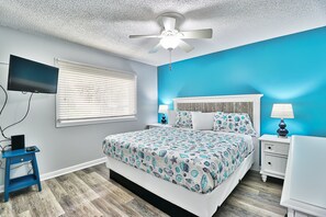 A bedroom with a bed, a ceiling fan, a TV, a nightstand, and a lamp.