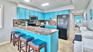 A modern kitchen with blue cabinets, a granite island, and a black refrigerator.
