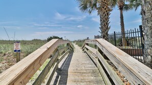 A wooden boardwalk leading to a beach, with a sign requesting to keep off dunes.