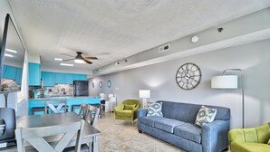 A modern living room with a blue sofa, green armchairs, and a dining area with a table and chairs.