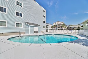 A swimming pool with a pool ladder, surrounded by a white fence, and adjacent to a building with multiple windows and balconies.