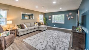 A living room with a sectional sofa, a coffee table, and a large rug. There are two windows with blinds, a lamp, and a mirror on the wall. - Spacious, Cozy 3 Bedroom 2 bath North End Home (Tacoma)