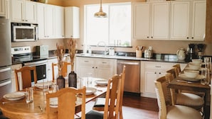 A kitchen with white cabinets, a dining table set with plates and glasses, and a hanging light fixture. - 3bdrm, 3bath in forest,  12 min to downtown Sequim,Wifi, Fire pit, Sauna, Hottub (Sequim)