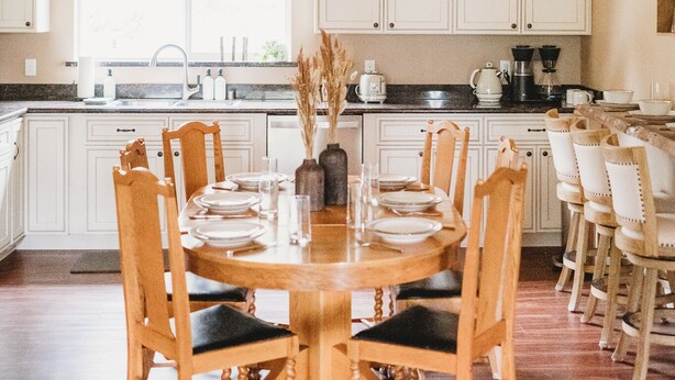 A wooden dining table with chairs, a kitchen in the background, and a ceiling with wooden beams. - 3bdrm, 3bath in forest,  12 min to downtown Sequim,Wifi, Fire pit, Sauna, Hottub (Sequim)