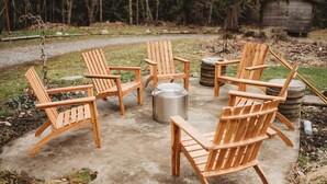 A concrete patio with four wooden Adirondack chairs arranged around a metal fire pit. - 3bdrm, 3bath in forest,  12 min to downtown Sequim,Wifi, Fire pit, Sauna, Hottub (Sequim)
