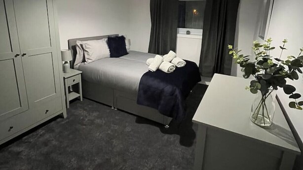 Una habitación compacta con cama, mesita de noche, armario y un pequeño escritorio con una planta.