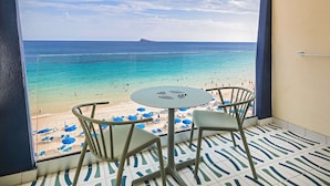 Un balcón con vista a una playa y al océano. Hay dos sillas y una mesa en el balcón.