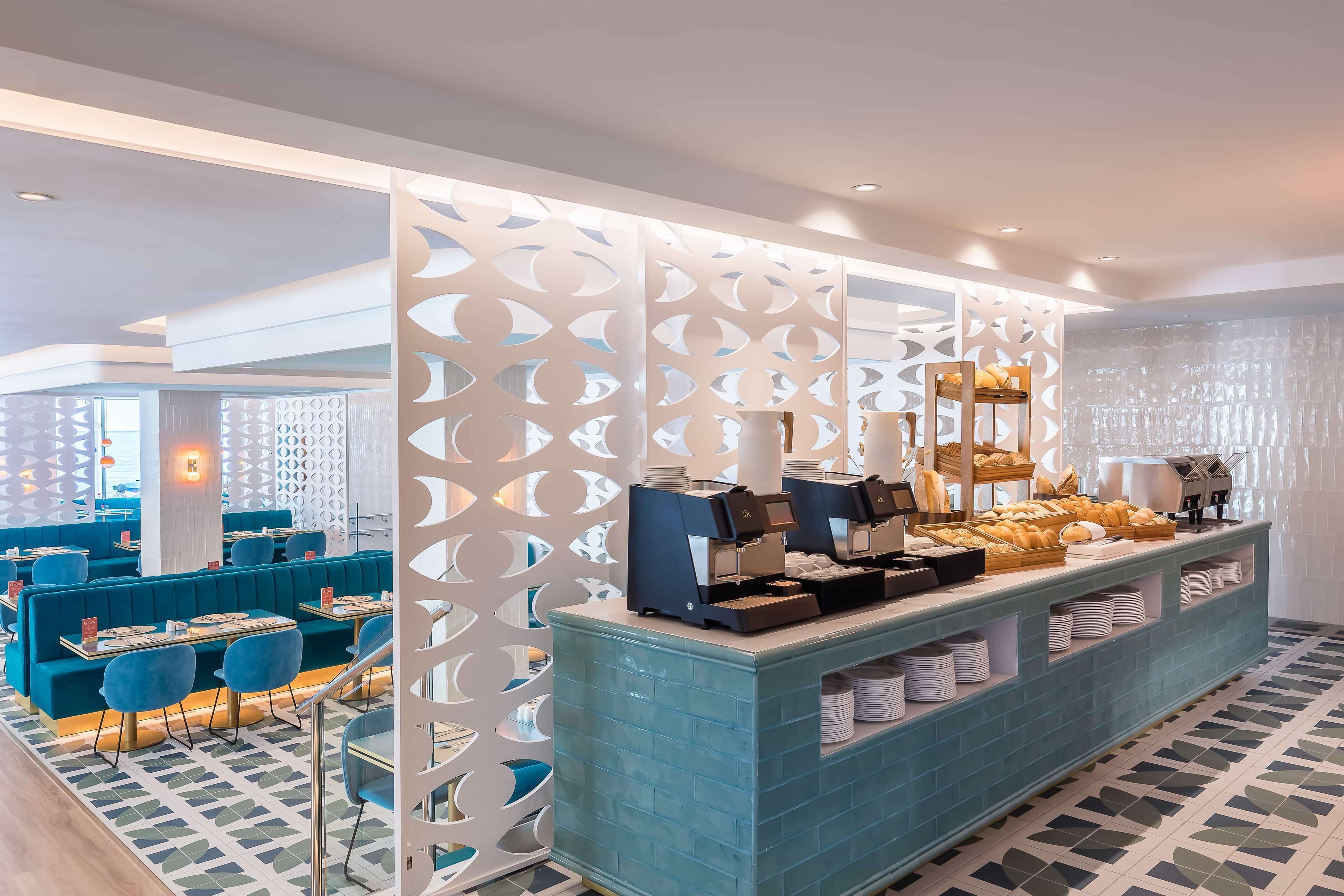 A modern restaurant with blue seating, a buffet counter with food and coffee machines, and decorative white partitions.