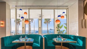 Un comedor moderno con asientos tipo banca tapizados en color turquesa, mesas de vidrio e iluminación colgante.