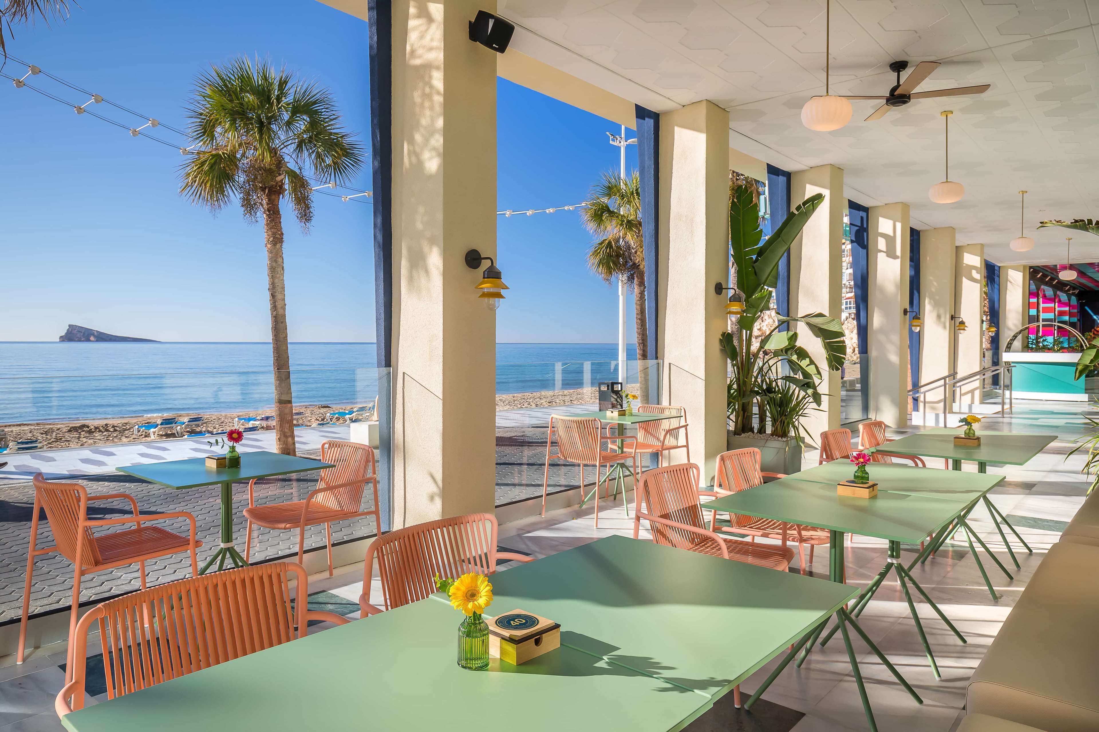 Un restaurante frente al mar con terraza, ventanas amplias y vistas al océano.