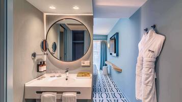 Une salle de bain moderne avec un grand miroir rond, un lavabo blanc et deux serviettes suspendues à des crochets.