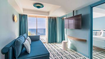 Una habitación de hotel moderna con un ventanal grande, un sofá, un televisor de pantalla plana y una cama con colcha de rayas azules y blancas.