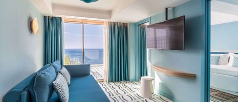Una habitación de hotel moderna con un ventanal grande, un sofá, un televisor de pantalla plana y una cama con colcha de rayas azules y blancas.