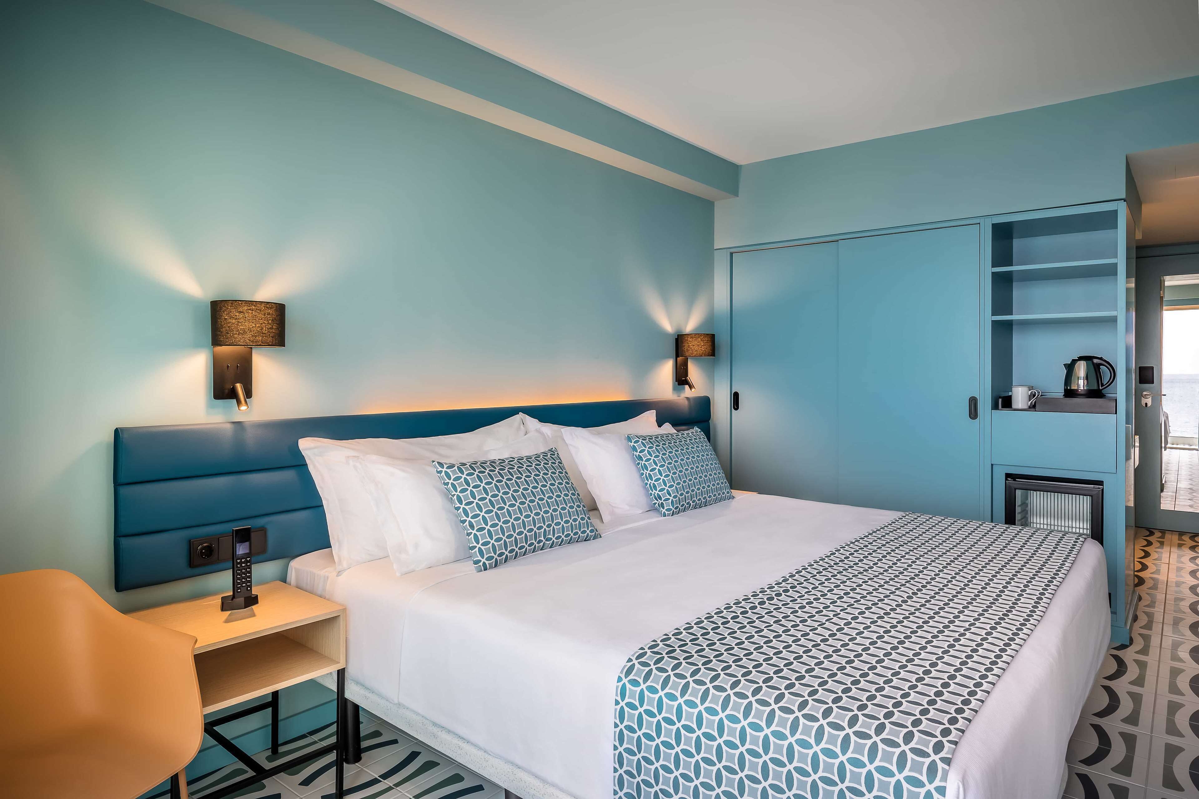 Quarto de hotel com cama, mesas de cabeceira, escrivaninha e guarda-roupa.