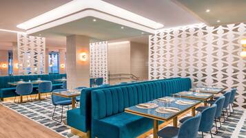 Un restaurante moderno con asientos tapizados en color turquesa y sillas azules, con paredes de diseño geométrico y suelo de baldosas.