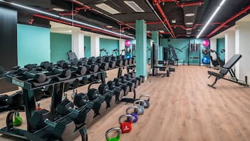 Un gimnasio con diverso equipamiento para levantamiento de pesas, incluyendo mancuernas y kettelbells, y máquinas de ejercicio.