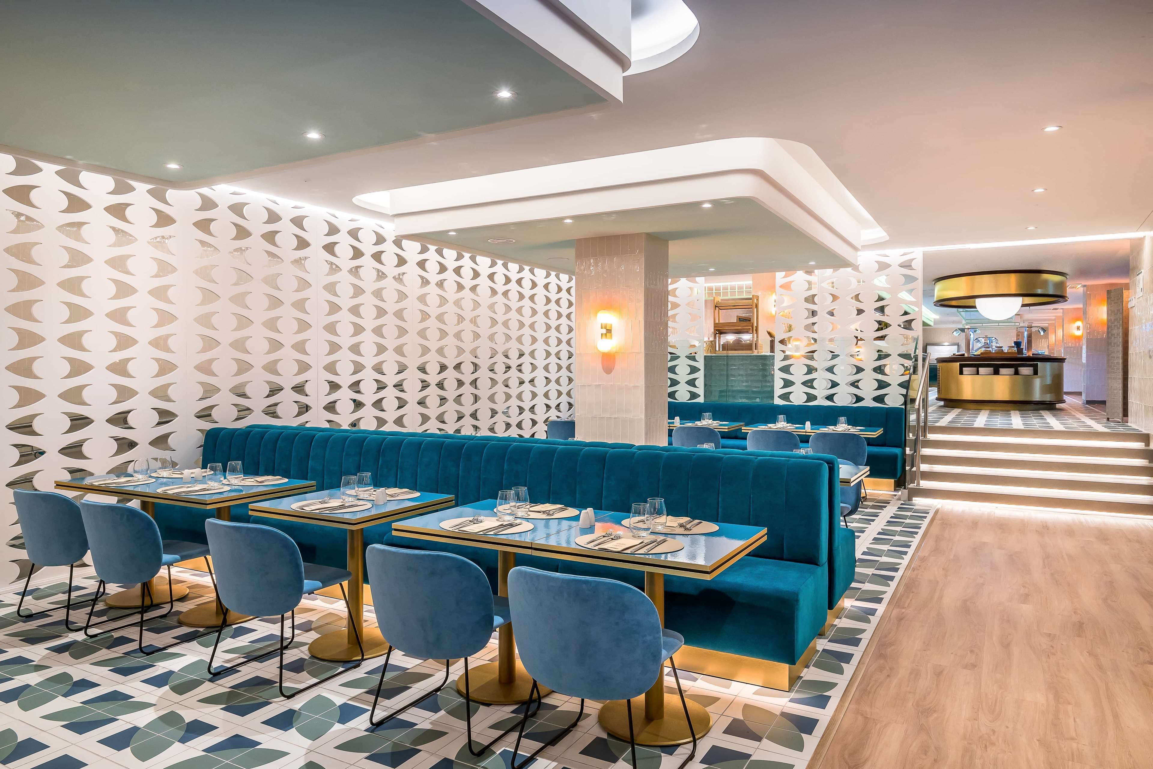 A modern restaurant with blue seating, geometric patterned walls, and a central bar area.