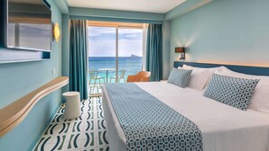 Habitación de hotel con una cama grande, televisor, vista al mar y una pequeña mesa con sillas.