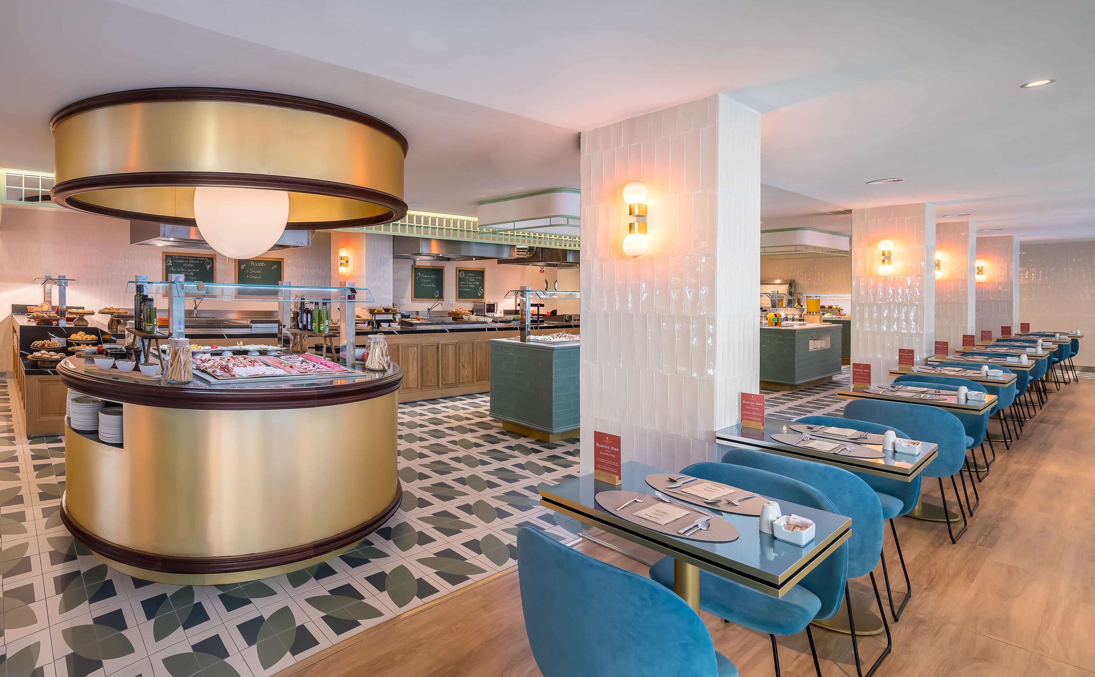 Un restaurante moderno con zona de bufé, sillas tapizadas en azul y suelo estampado.