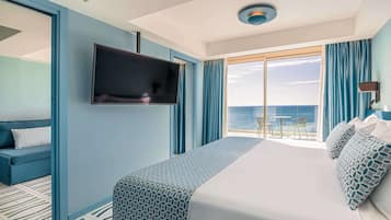 Een hotelkamer met een bed, een televisie, een balkon met een tafel en stoelen en uitzicht op zee.