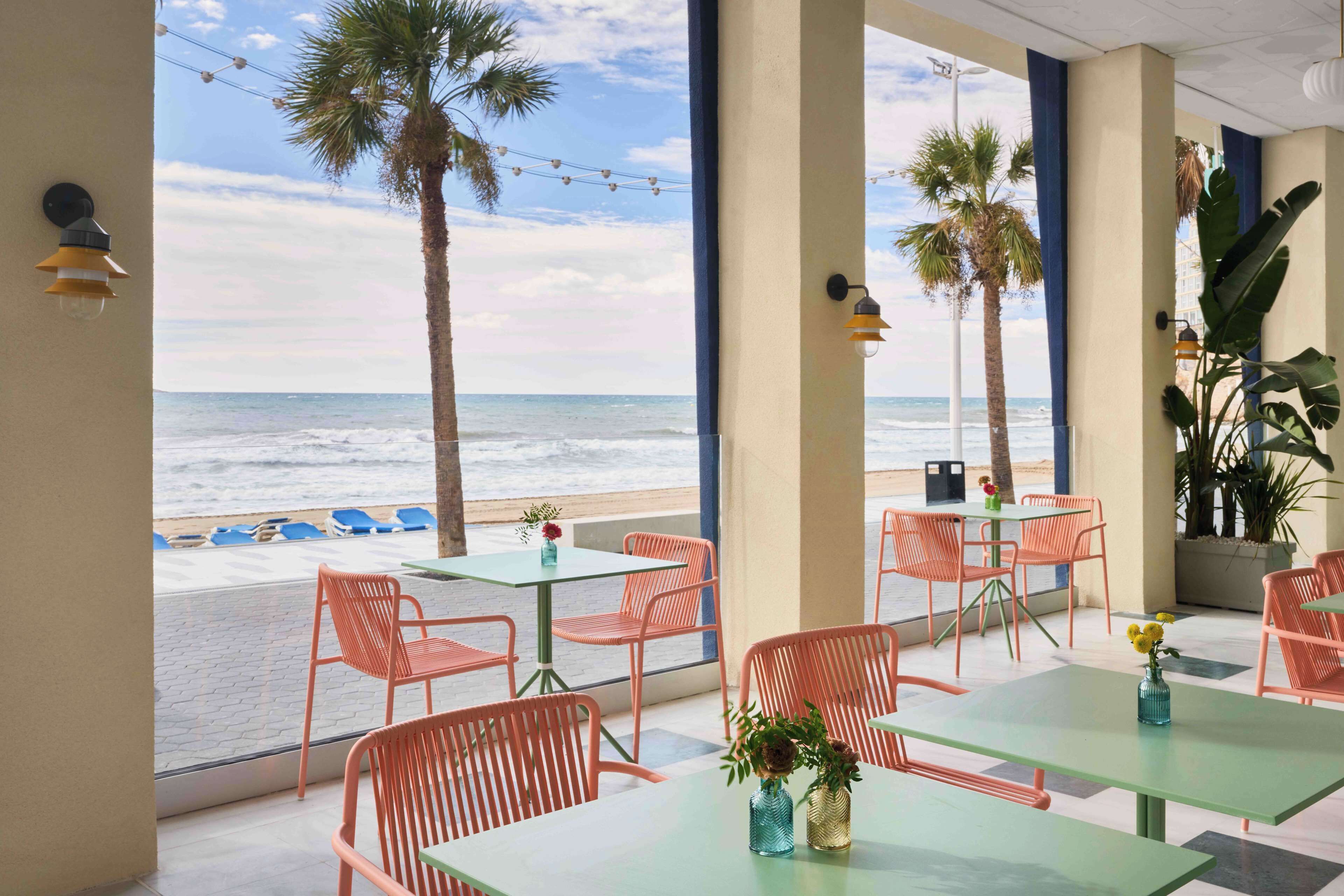 Un café frente a la playa con terraza, palmeras y vistas al océano.