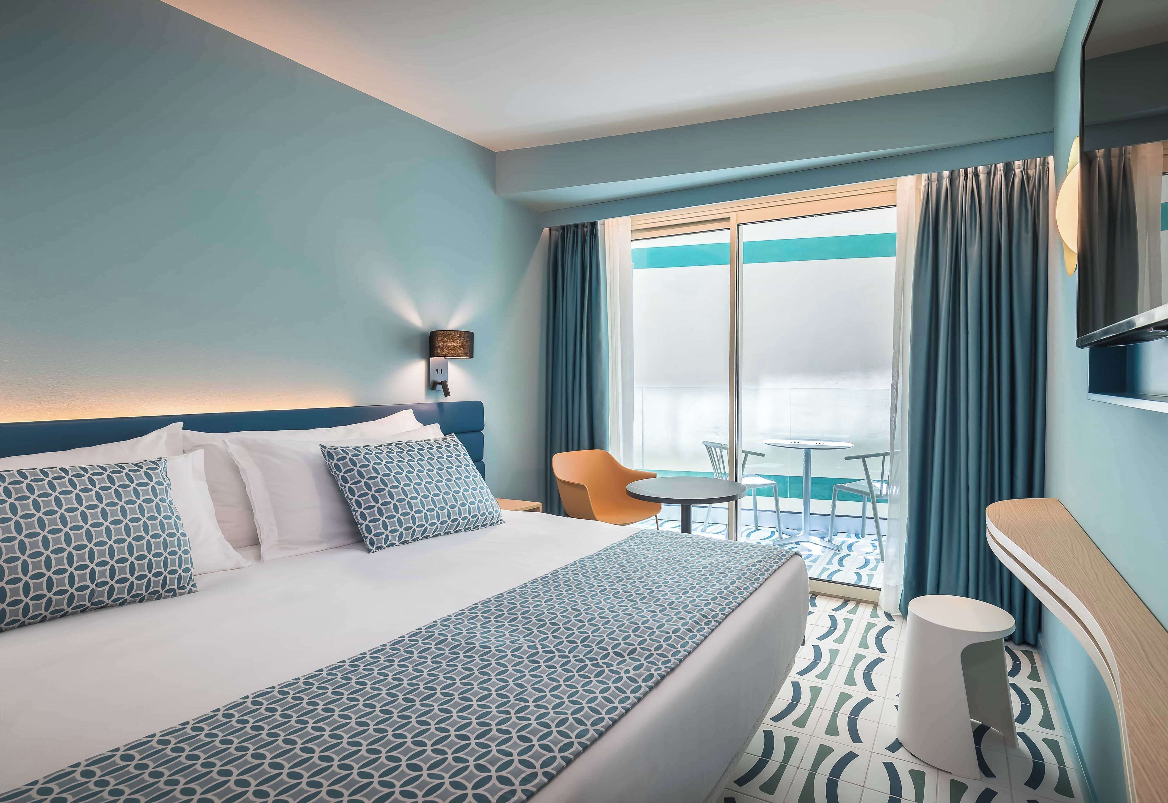 Ein Hotelzimmer mit Bett, kleinem Tisch, Stuhl und Blick ins Freie.