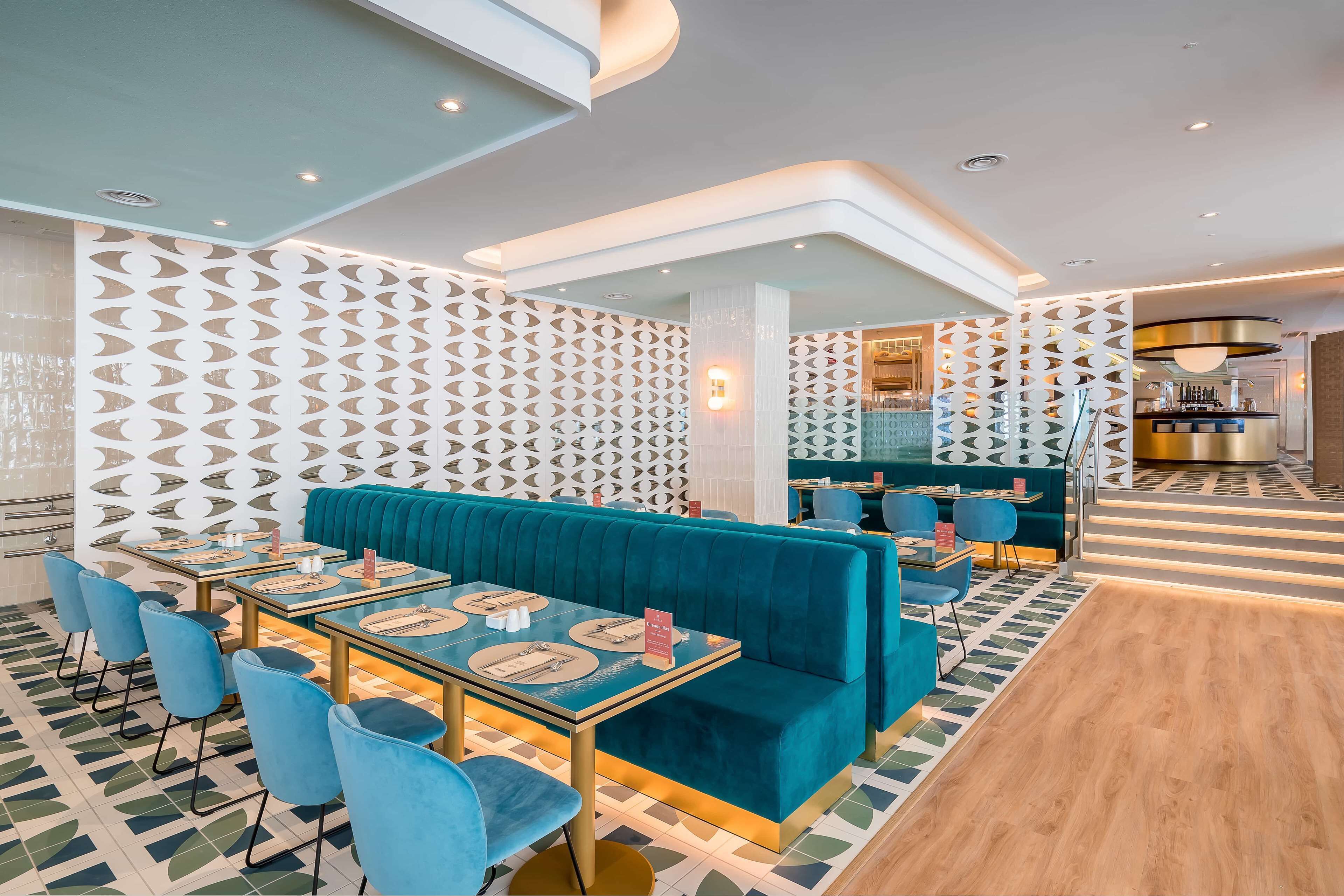 Un restaurant moderne avec des sièges de couleur turquoise, des murs ornés de motifs géométriques et un espace bar.