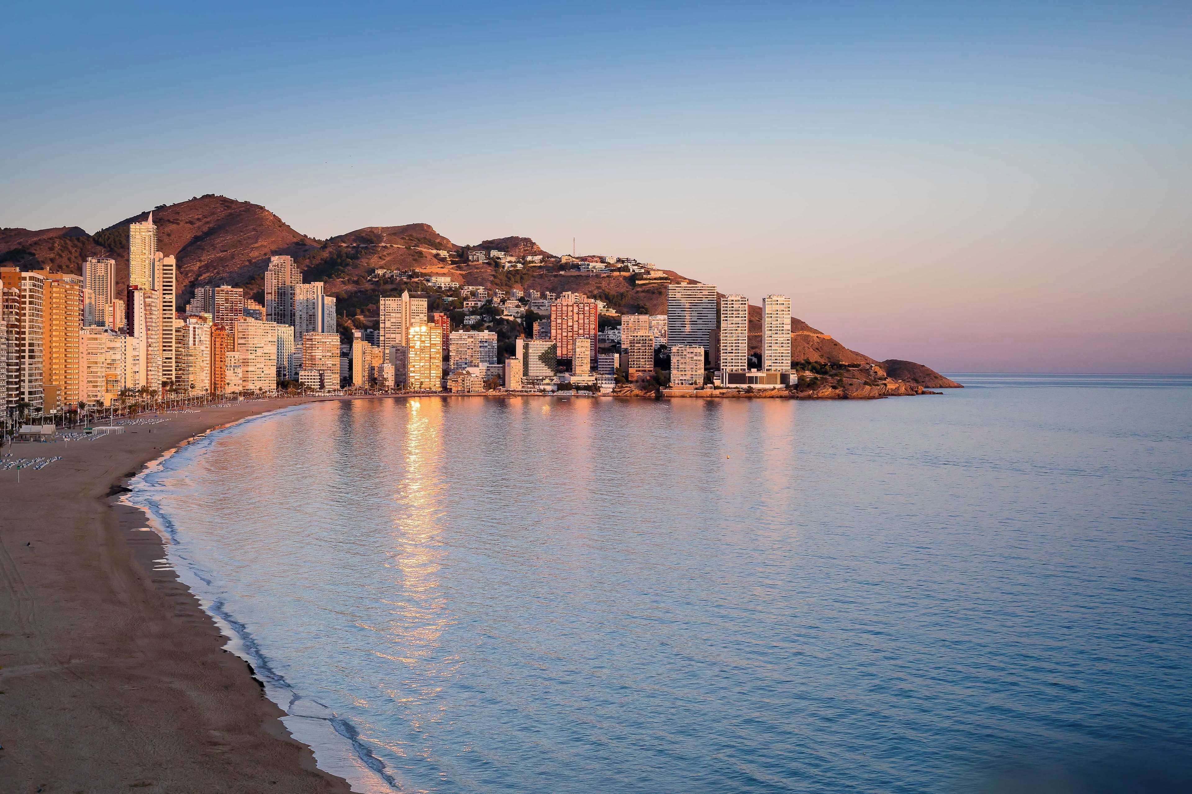 Un paisaje urbano costero con rascacielos a lo largo de la playa, una playa de arena y un mar tranquilo.